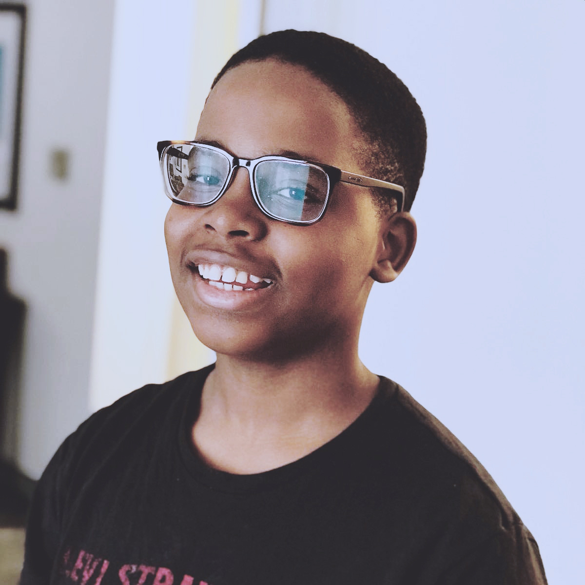 Young African American student with short dark hair, wearing glasses and a black t-shirt. He is smiling.