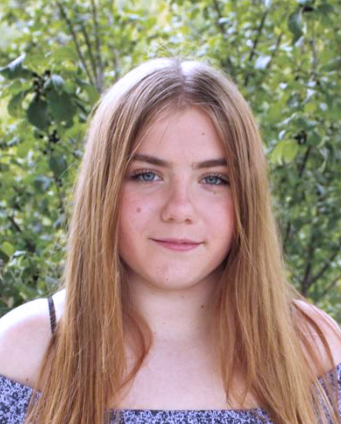 Young blonde college student standing in front of a background of trees. Close up with blue floral shirt off the shoulders.